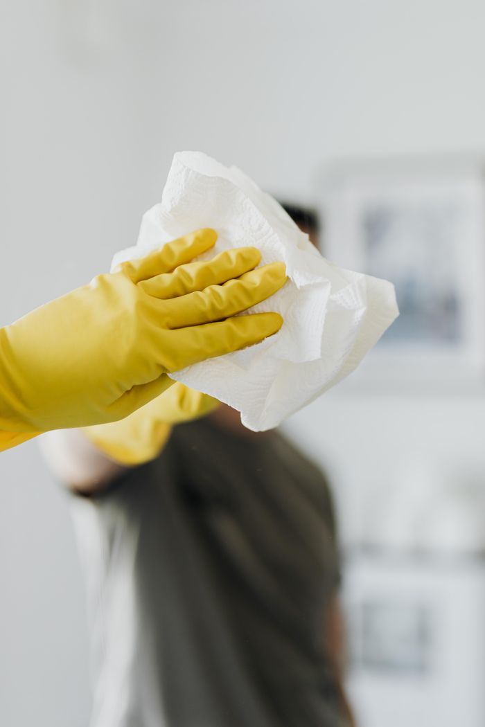 hero-img Anonymous male wearing yellow latex gloves and dark t shirt wiping mirror in bathroom with paper napkin