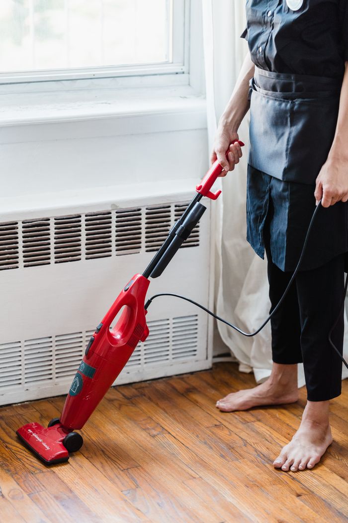 services-01 Person cleaning wooden floor with red vacuum cleaner in a well-lit room.